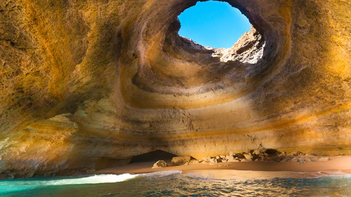 Speedboat cutting past golden limestone cliffs on the way to the Benagil sea cave in Portimão, Algarve, Portugal