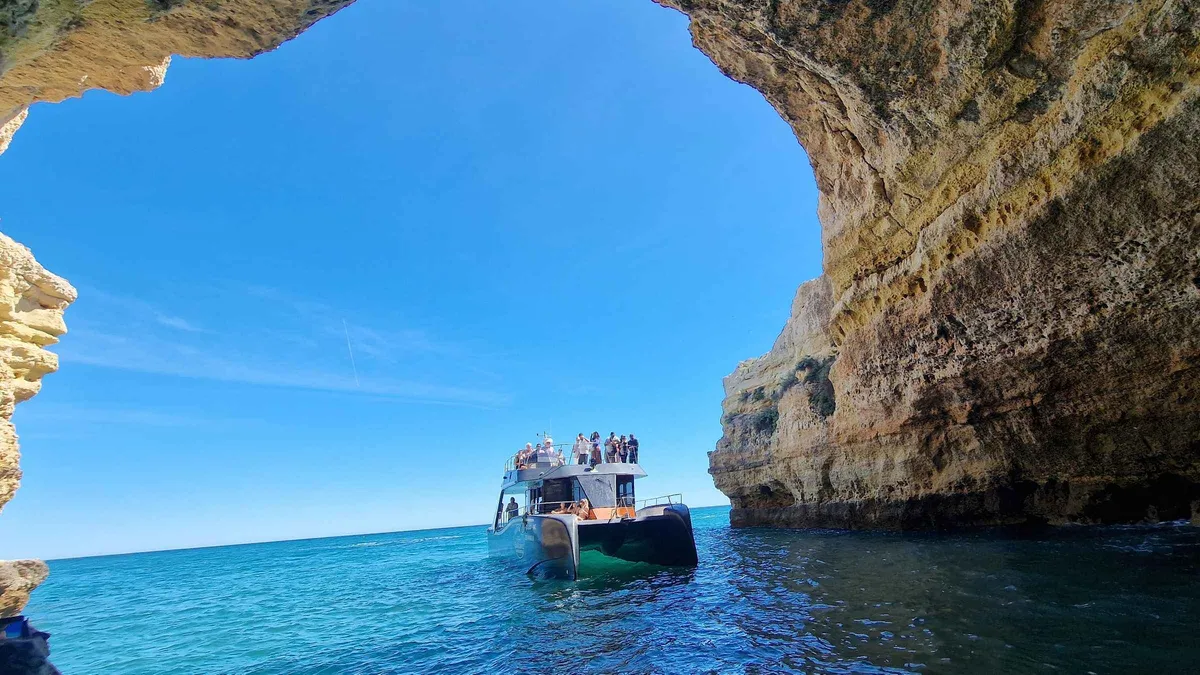 Catamaran anchored below ochre cliffs on the coastal run from Albufeira to the Benagil sea cave in the Algarve, Portugal