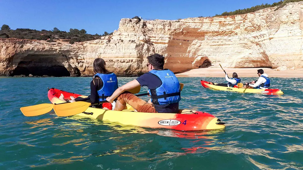 Guided kayakers paddling through a rock arch beside the Benagil sea cave on the Algarve coast, Portugal