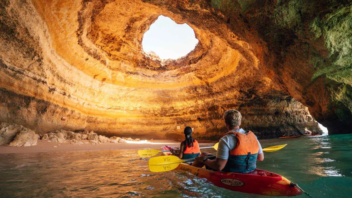 Double kayak entering a narrow sea cave on the paddle route to the Benagil sea cave in the Algarve, Portugal